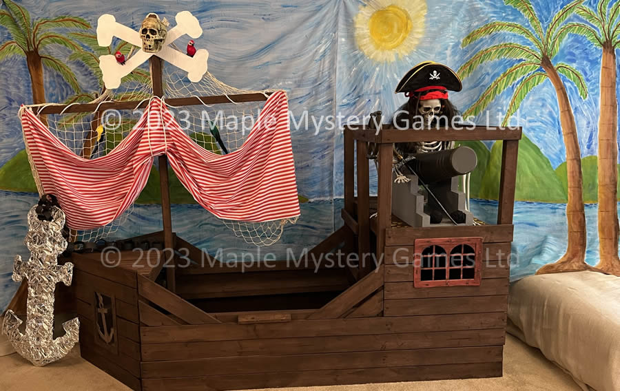 Pirate ship forms centre part of our murder mystery decorations - skull and crossbones atop the mast, skeleton in pirate outfit firing the canon, hand-painted palm tree backdrop